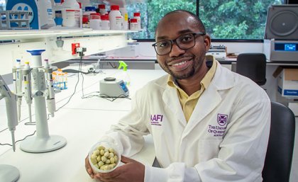 a man in a white lab coat sits at a bench holding a container of small round green fruit